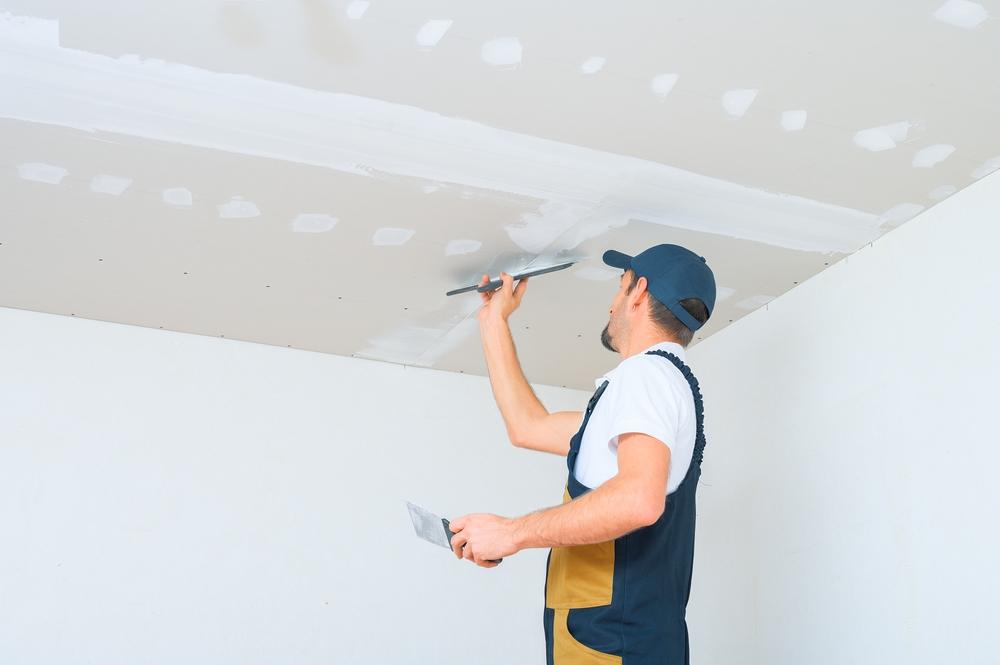 ouvrier en uniforme qui applique de l'enduit au plafond